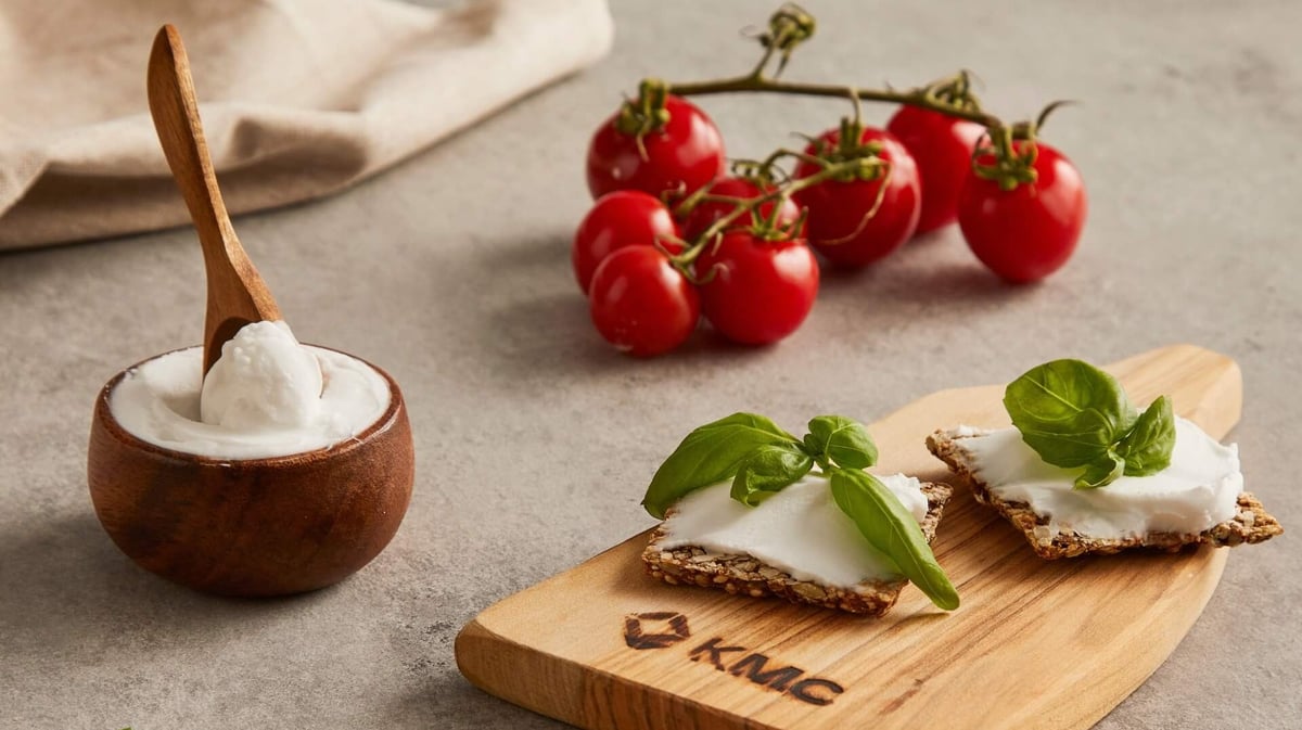 Cheese spread in a bowl with tomatoes and crisp bread on a breadboard